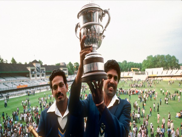 Two cricketers celebrating with a large trophy on the field after a big win.